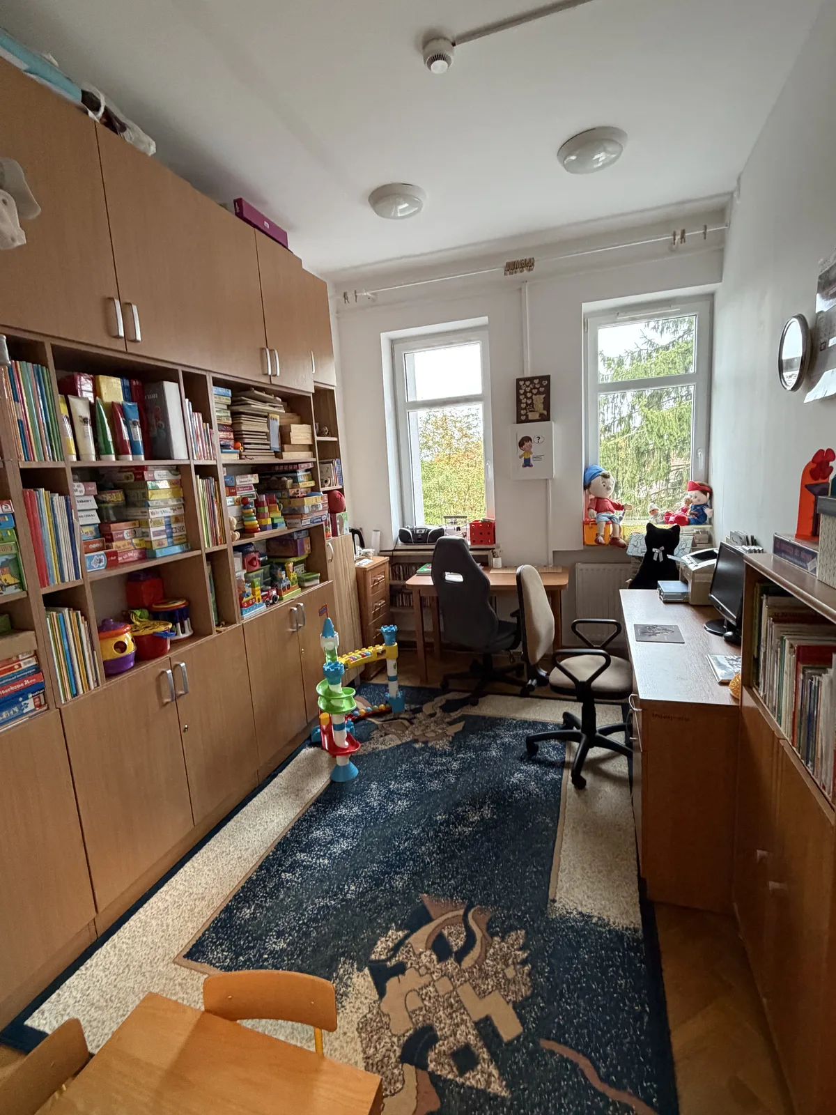 Gabinet terapii pedagogicznej: regały z pomocami dydaktycznymi i grami, dwa biurka ze stanowiskami do pracy indywidualnej z dzieckiem.