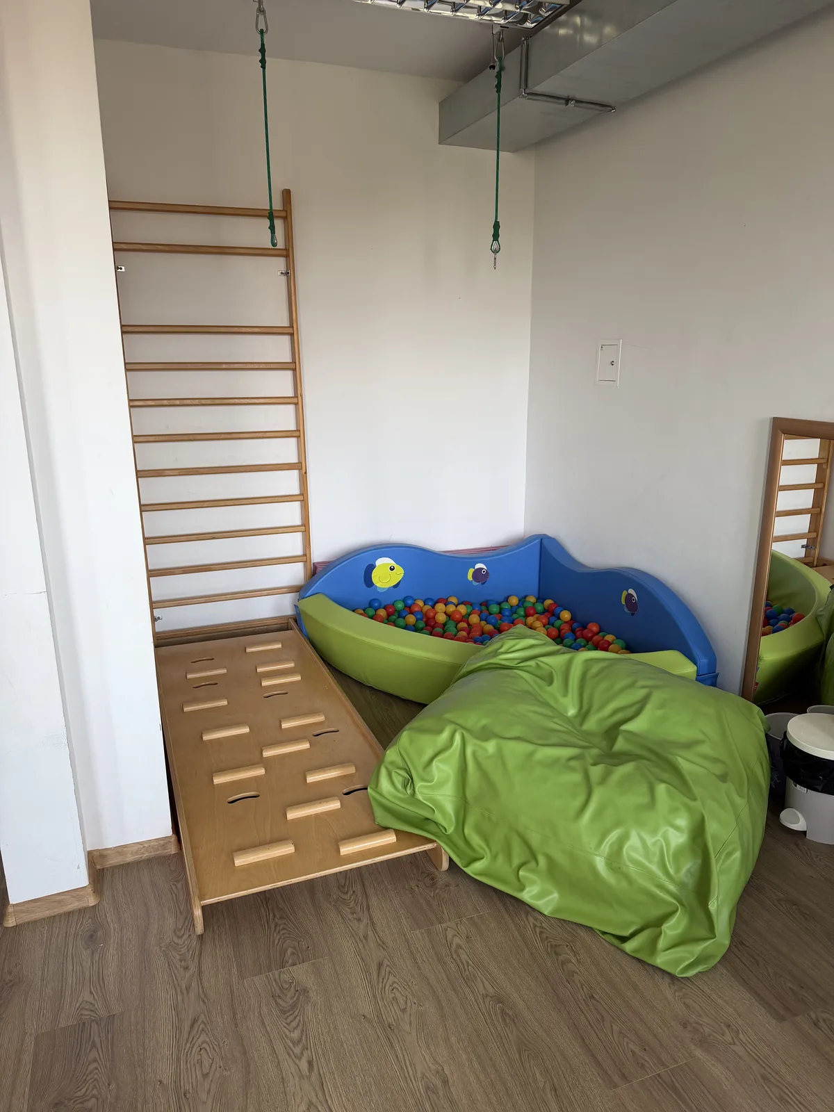 Gabinet Integracji Sensorycznej: suchy basen z kolorowymi kulkami, drabinka gimnastyczna, równoważnia z drewnianymi przeszkodami i miękka pufa.